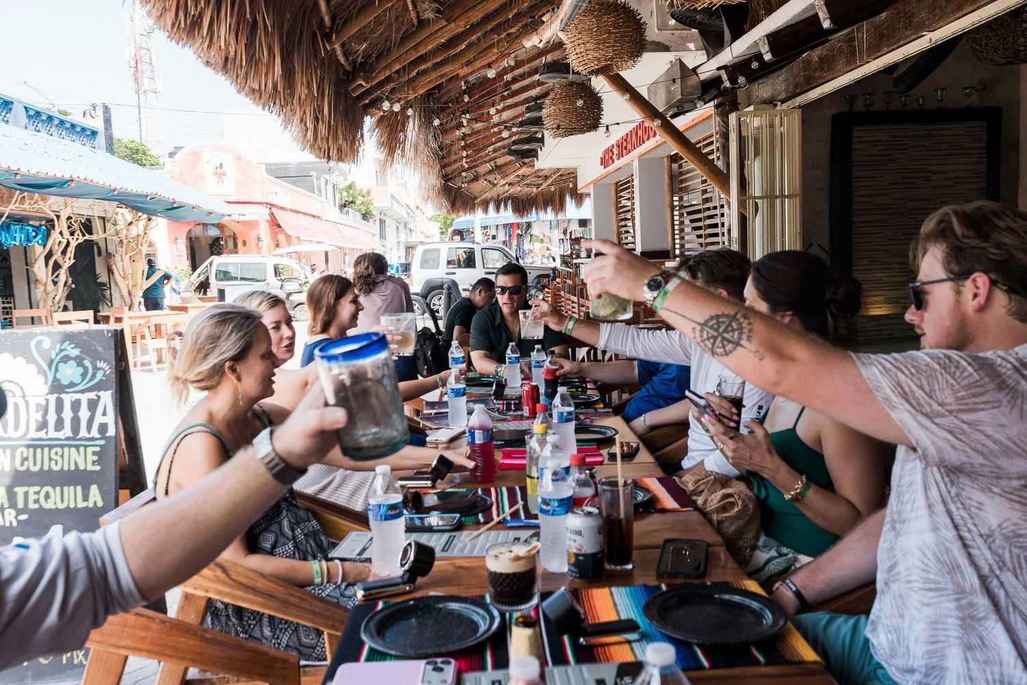 Riviera Maya Multi Day wedding - Group of friends toasting drinks at a long outdoor table at a Mexican restaurant