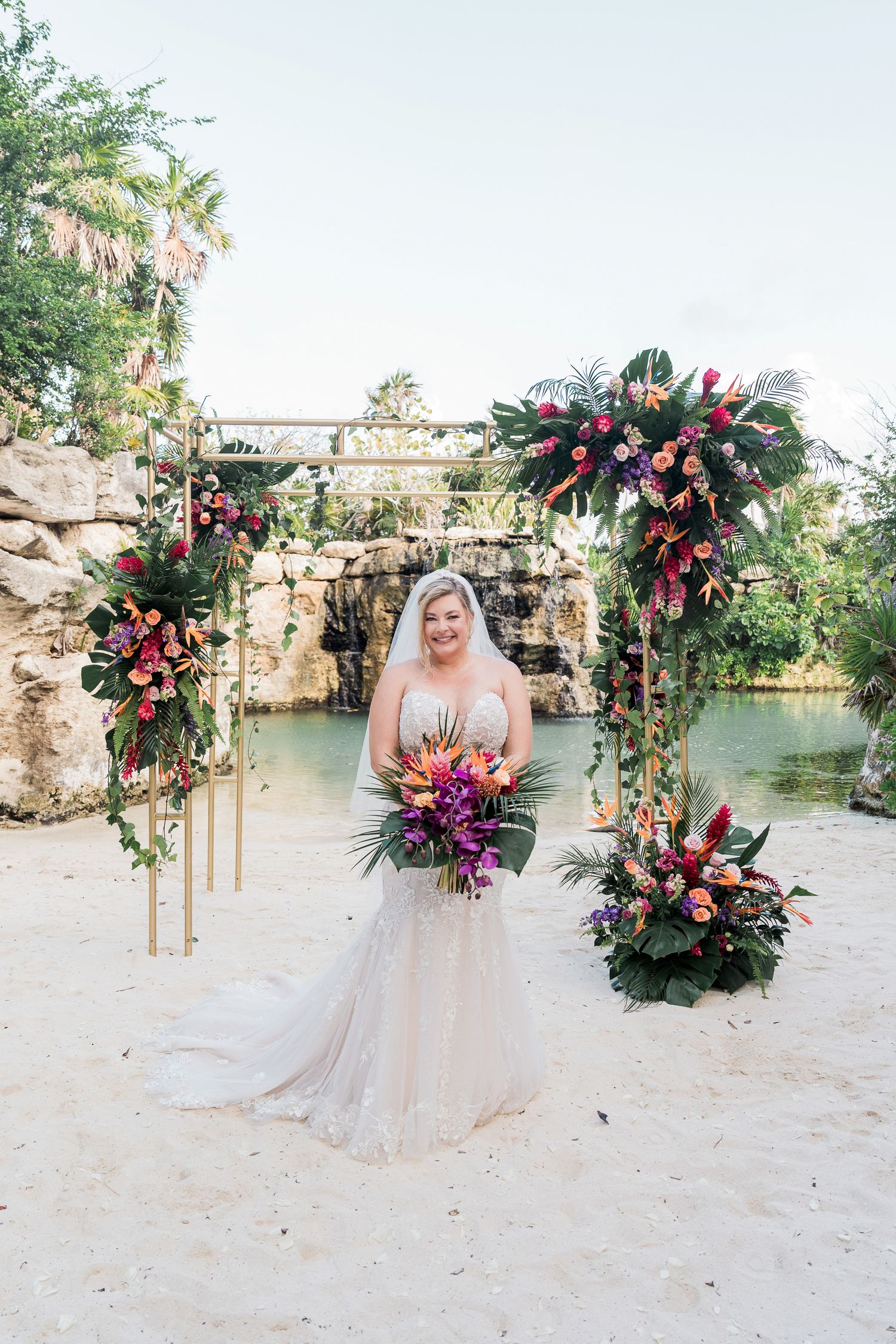 Hotel Xcaret México Wedding - Bride in lace gown and veil holds tropical bouquet with turquoise water backdrop.
