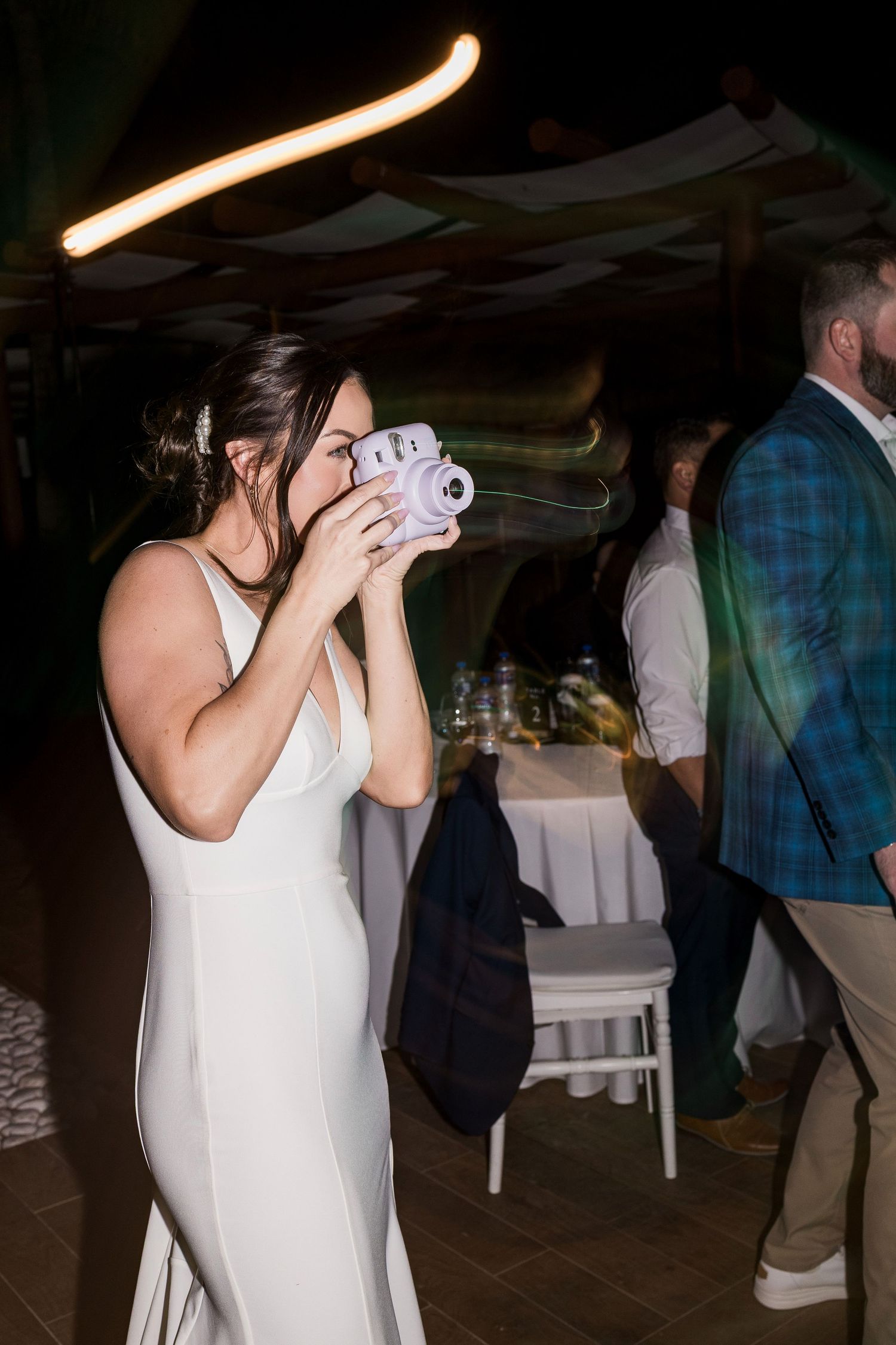 Bride in white gown uses Instax camera at wedding reception party.