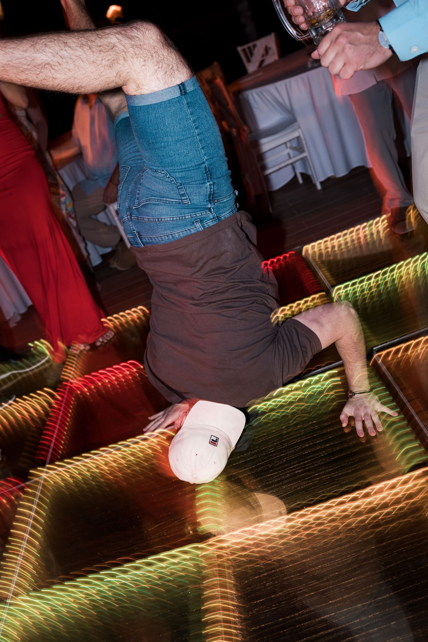 Man doing a headstand on illuminated dance floor at a lively party event.
