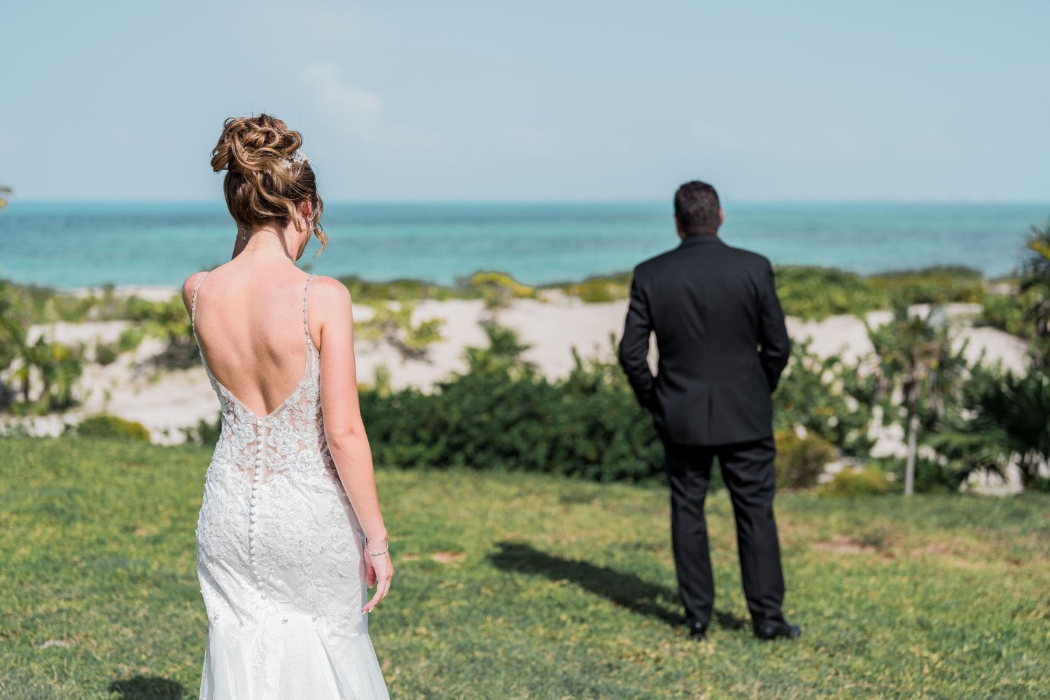 Bride and groom first look moment on lawn with ocean backdrop.