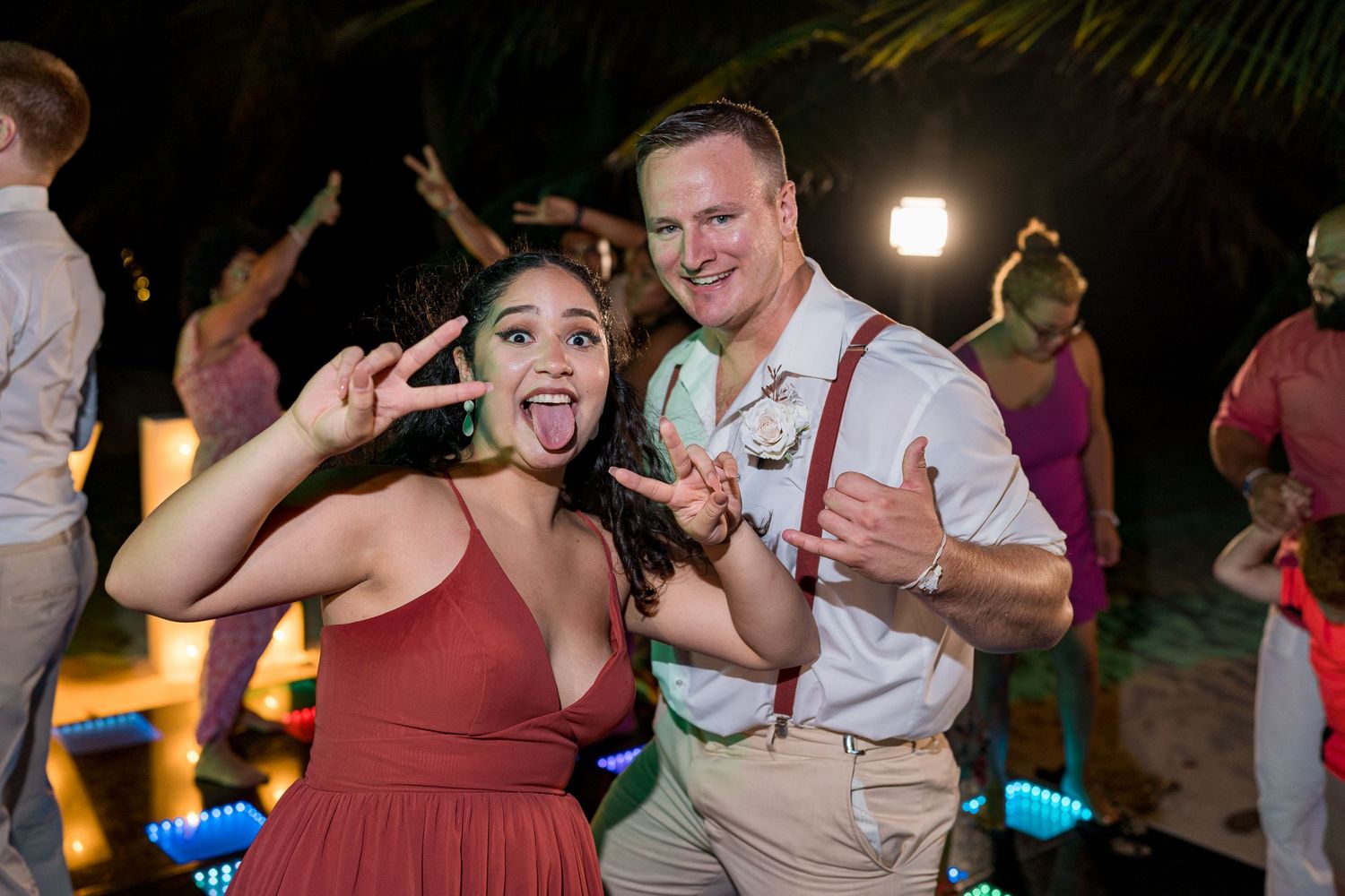 Couple posing playfully with peace signs at outdoor wedding reception at night.