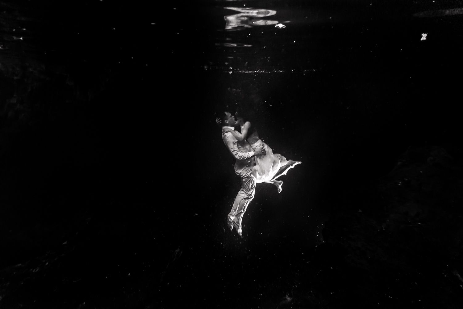 Black and white underwater photo of bride swimming in wedding dress.