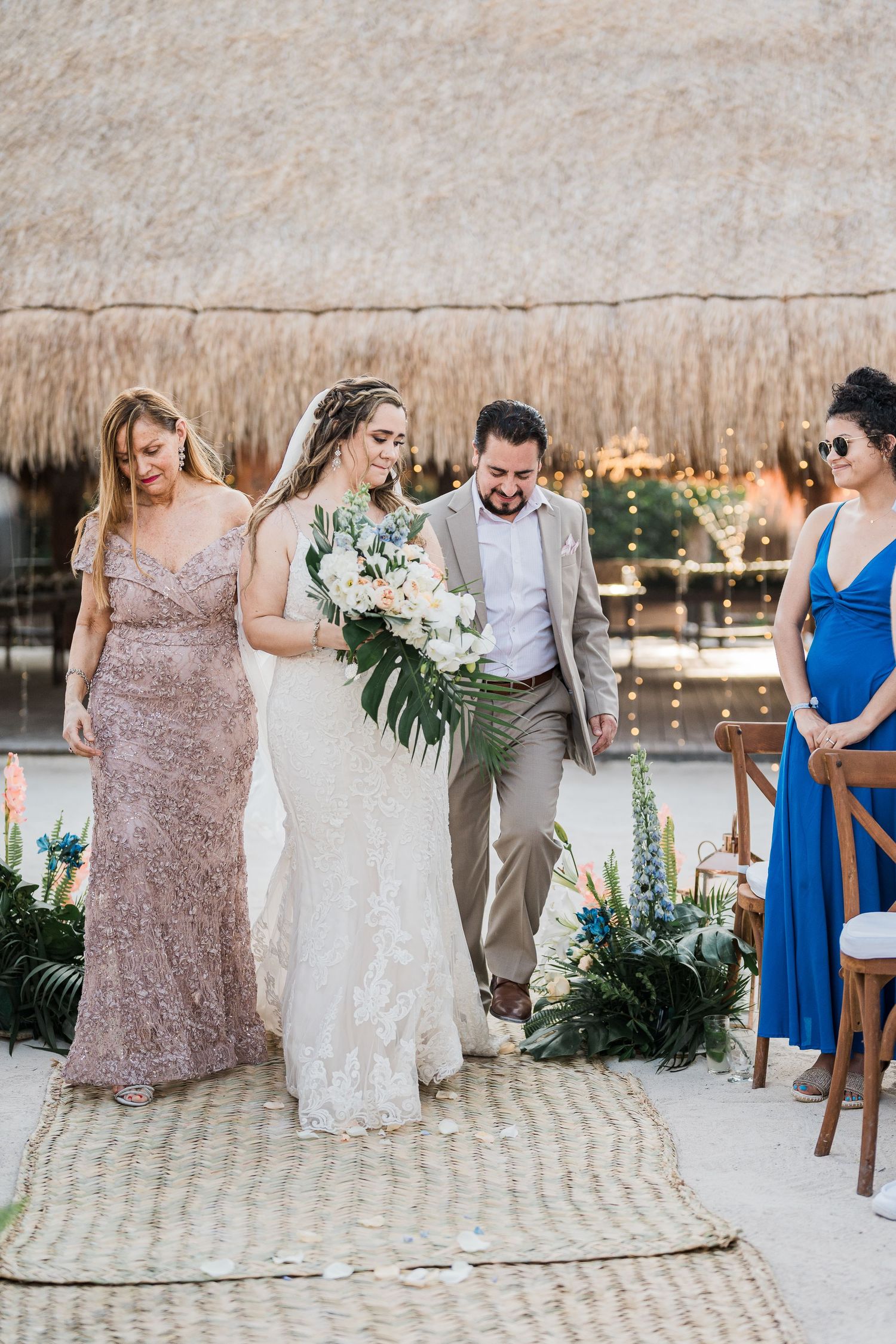 Bride walks down the aisle with parents at a tropical beach wedding ceremony.