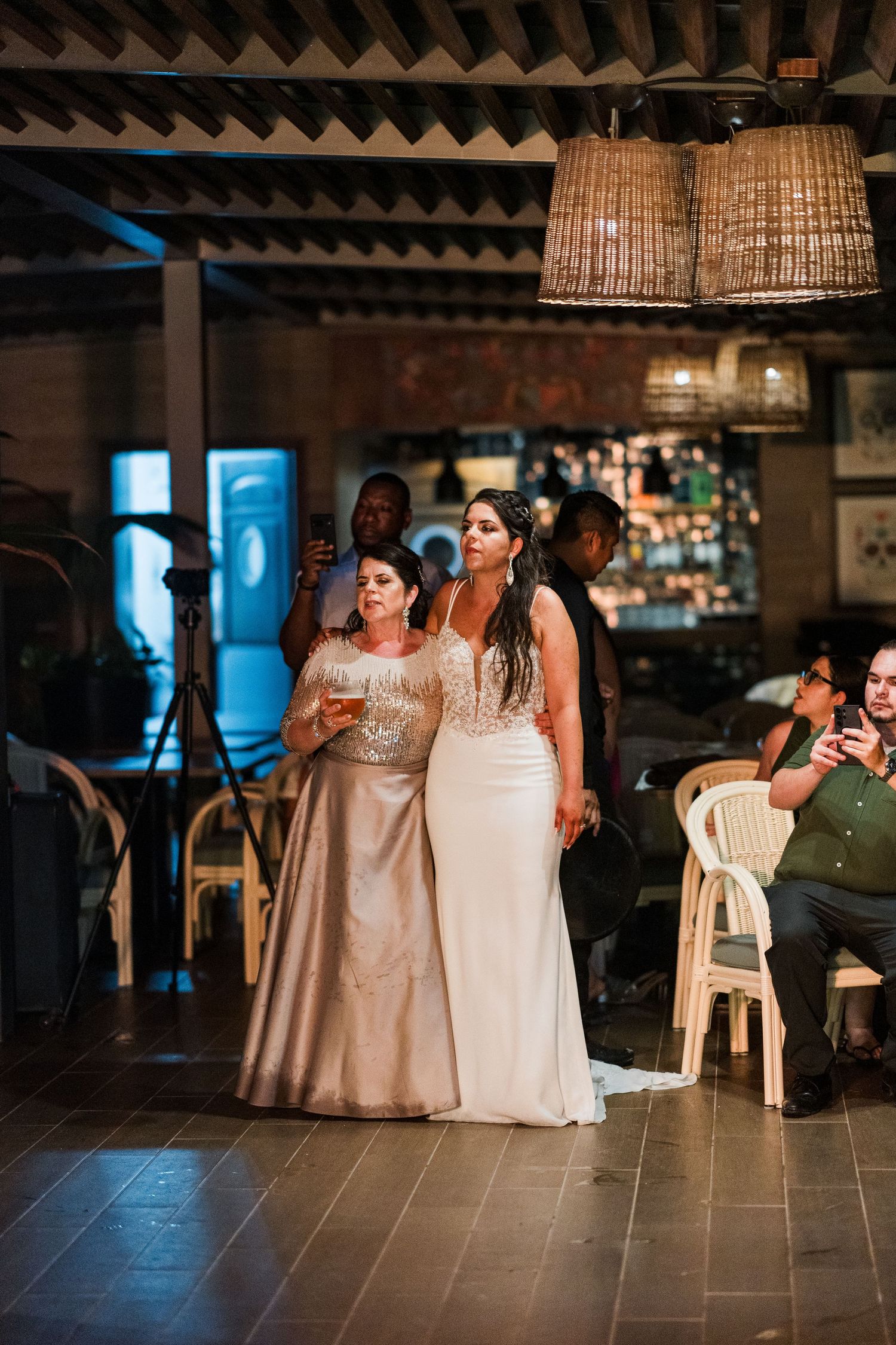 Bride stands with elegantly dressed woman holding champagne during heartfelt wedding reception moment.