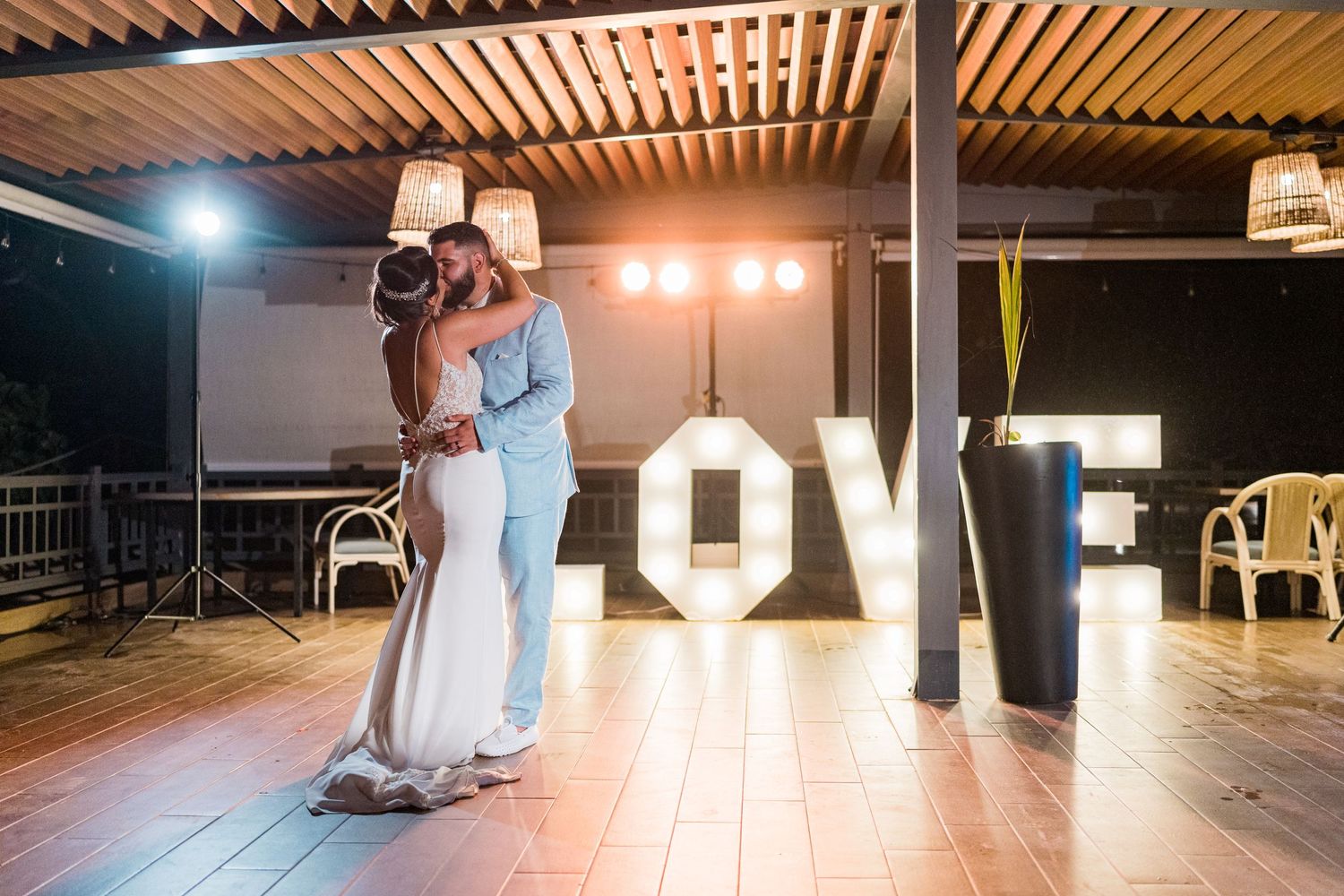 Newlyweds share a romantic first dance beside a glowing LOVE sign at their beach wedding reception.