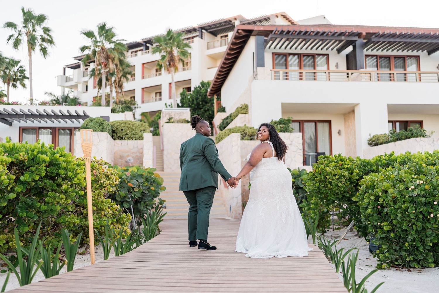 Bride and groom holding hands on wooden boardwalk at tropical resort wedding venue.