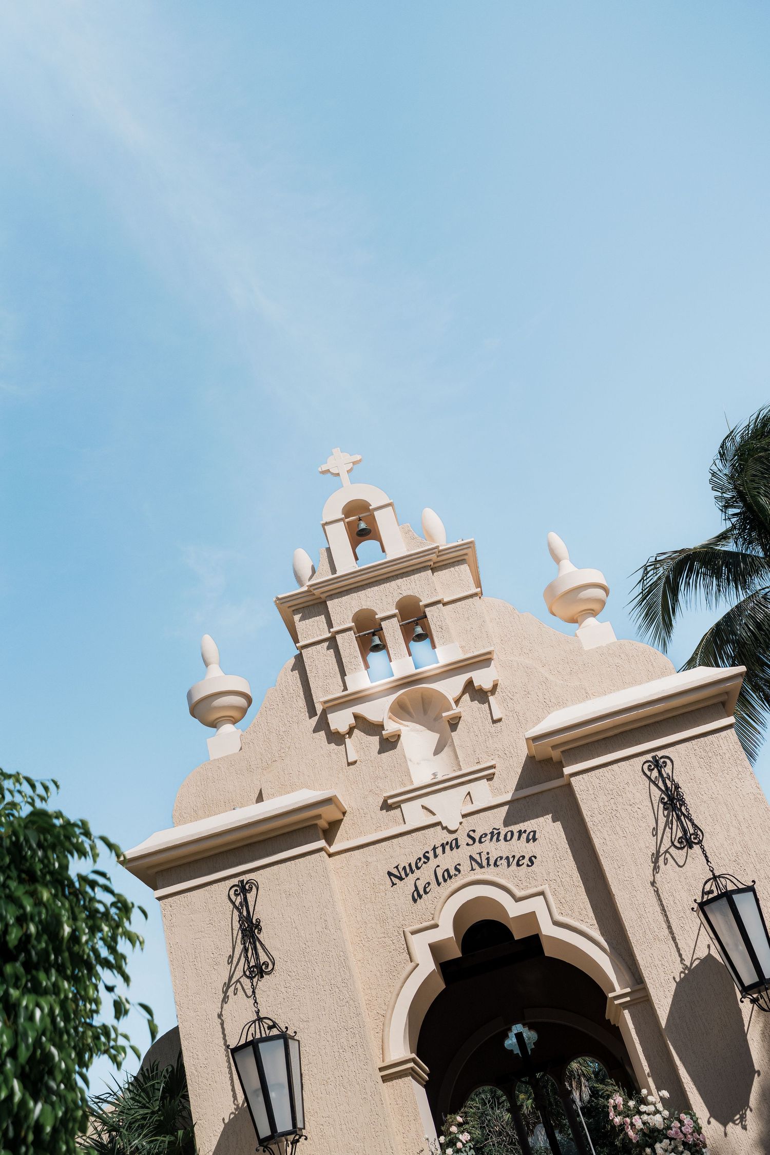 Nuestra Señora de las Nieves church facade with bell tower, ornate details, and palm trees under blue sky.