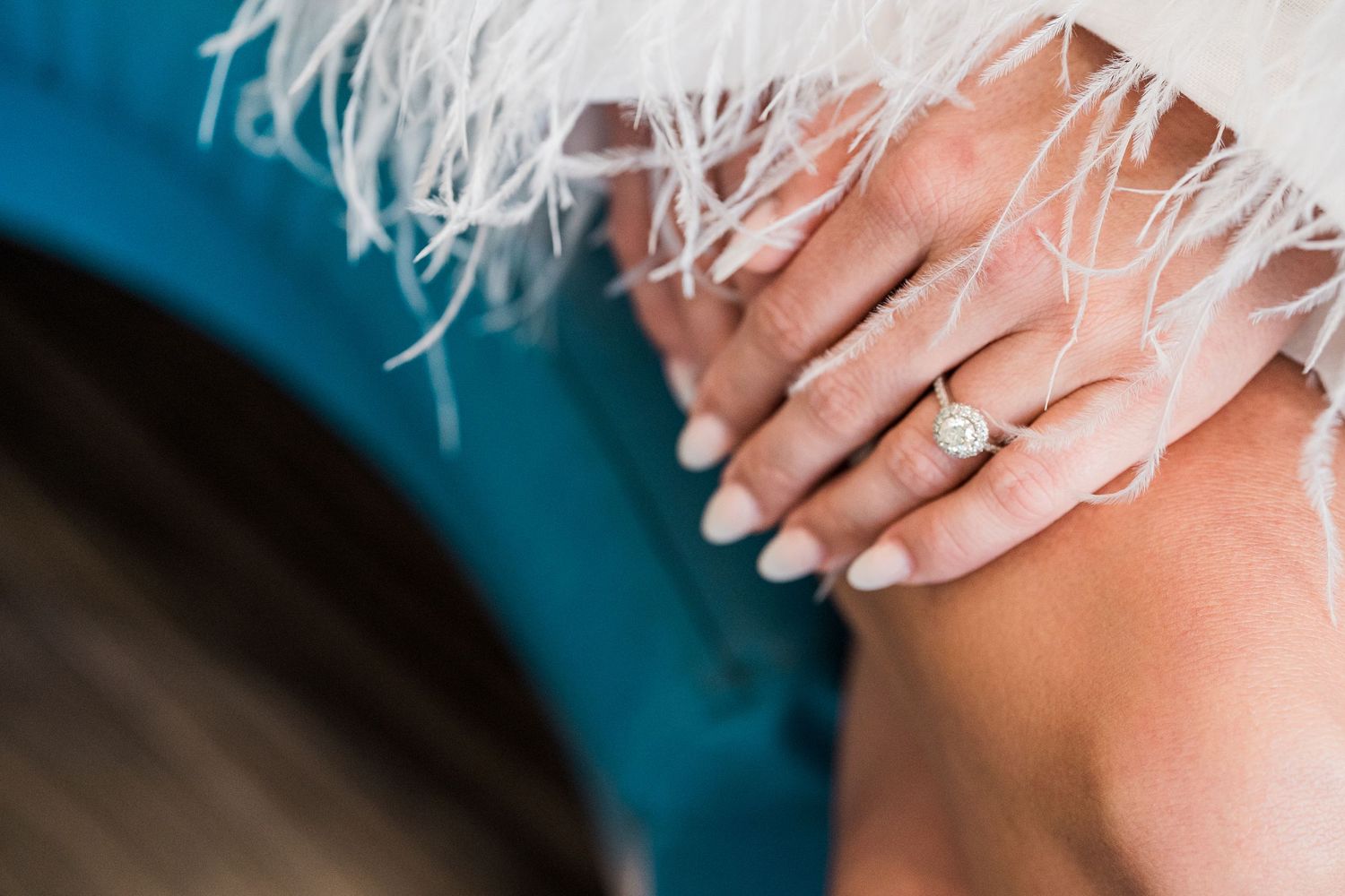 Close-up of a woman's hand wearing an elegant diamond halo engagement ring with white manicured nails.