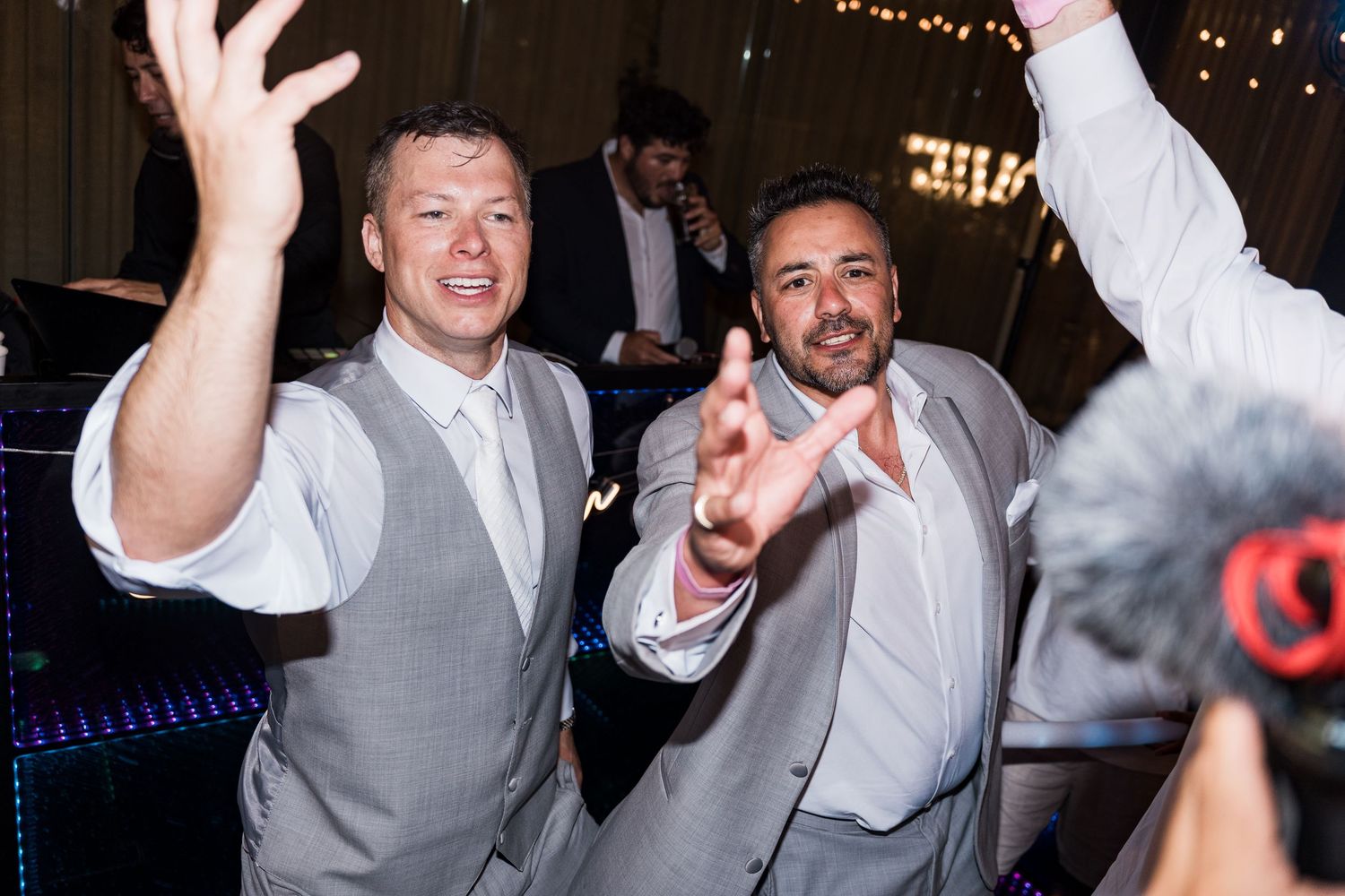 Two men in gray suits dancing joyfully at a wedding reception celebration.