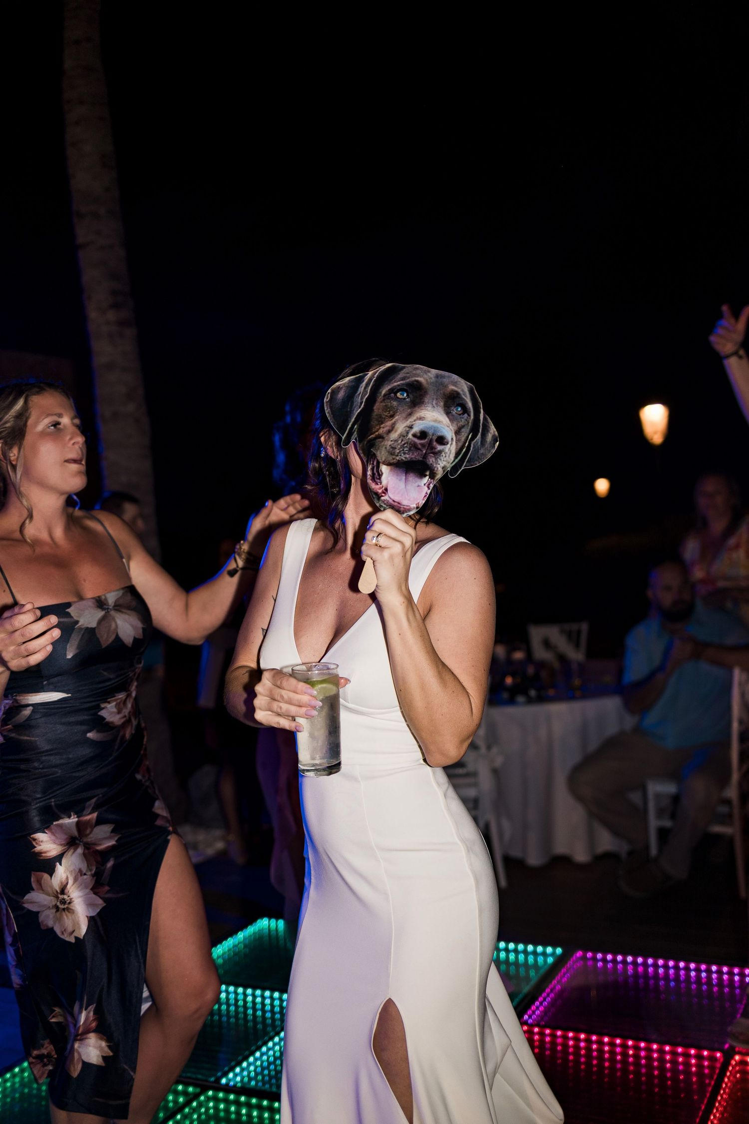 Bride wearing a dog face mask while dancing at her wedding reception under colorful LED lights.