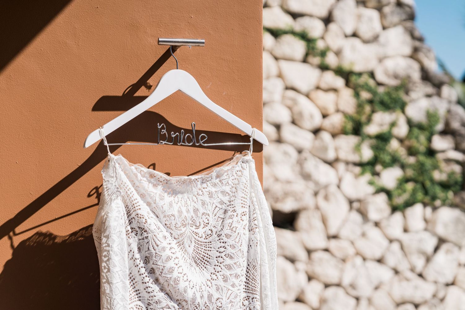Xcaret Arte Wedding - White lace wedding dress on a decorative Bride hanger against a rustic stone and terracotta wall.