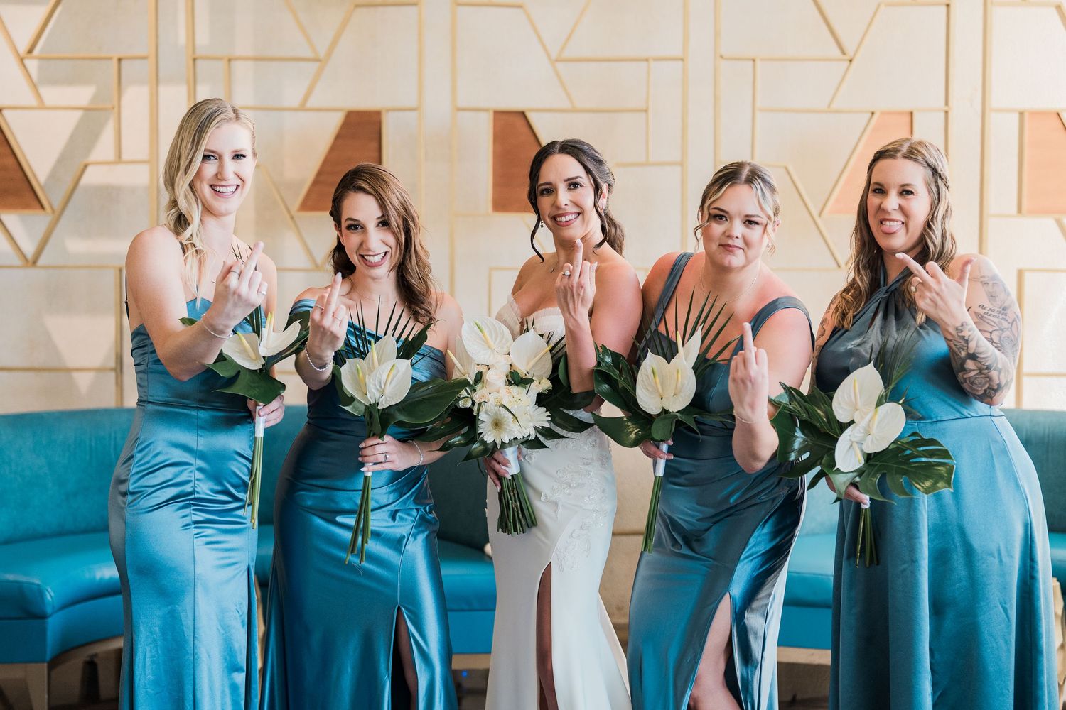 Bride in white gown poses with four bridesmaids in teal satin dresses holding white bouquets indoors. grand palladium costa mujeres wedding