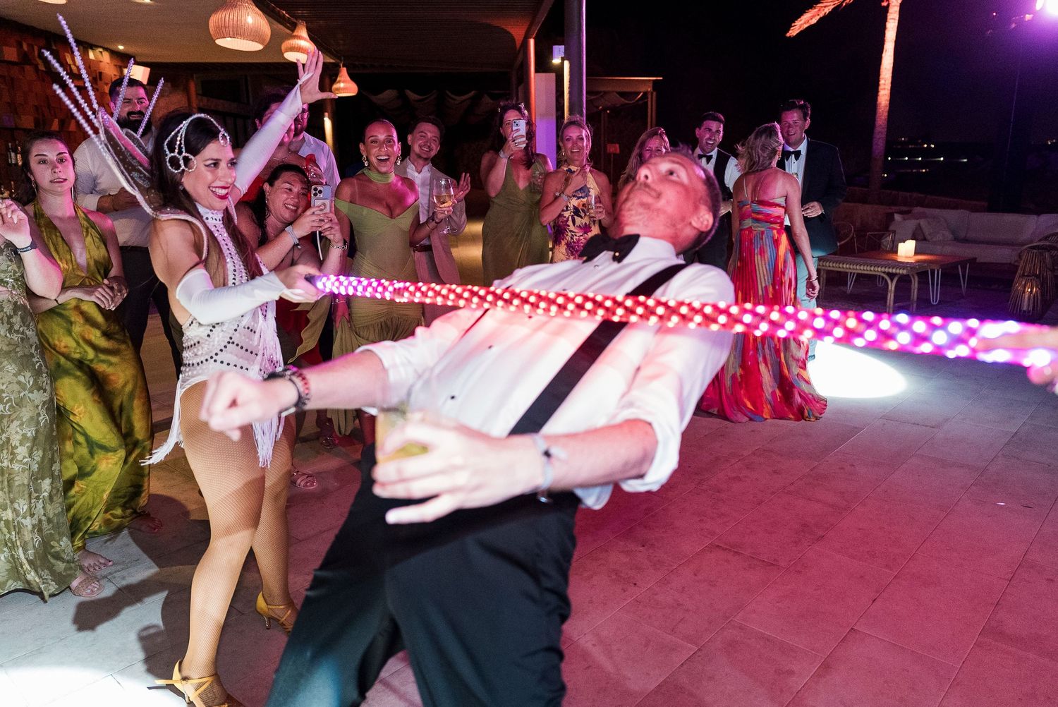 Man doing the limbo dance at a lively wedding reception party with guests cheering in the background.