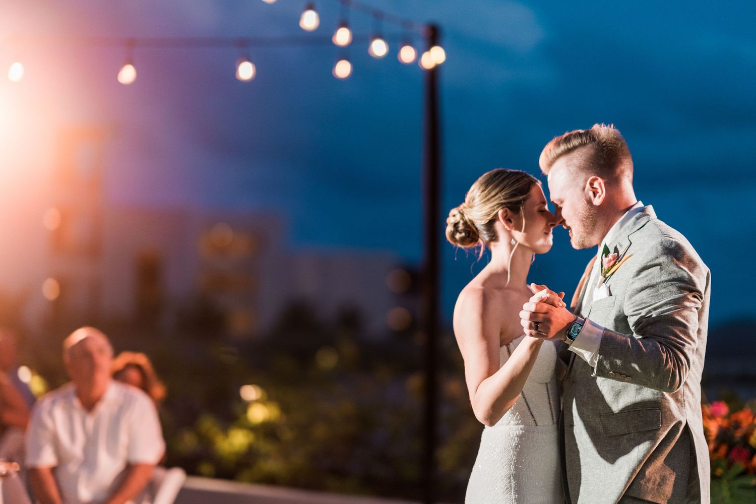 Couple sharing first dance under string lights at outdoor evening wedding reception.