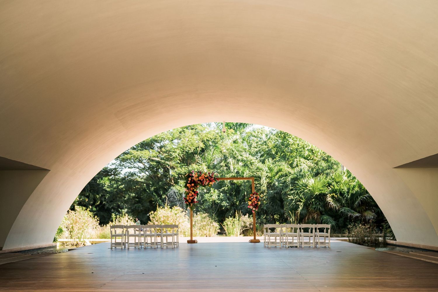 Secrets Akumal Wedding - Elegant outdoor wedding venue with arched white ceiling, wooden floor and floral arch