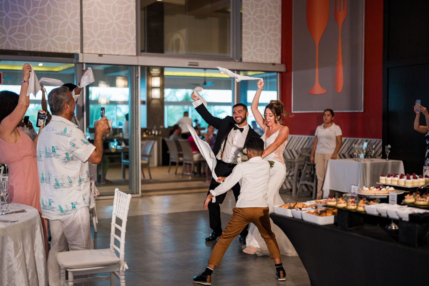 Excited wedding guests celebrate with raised arms as bride and groom make their reception entrance.