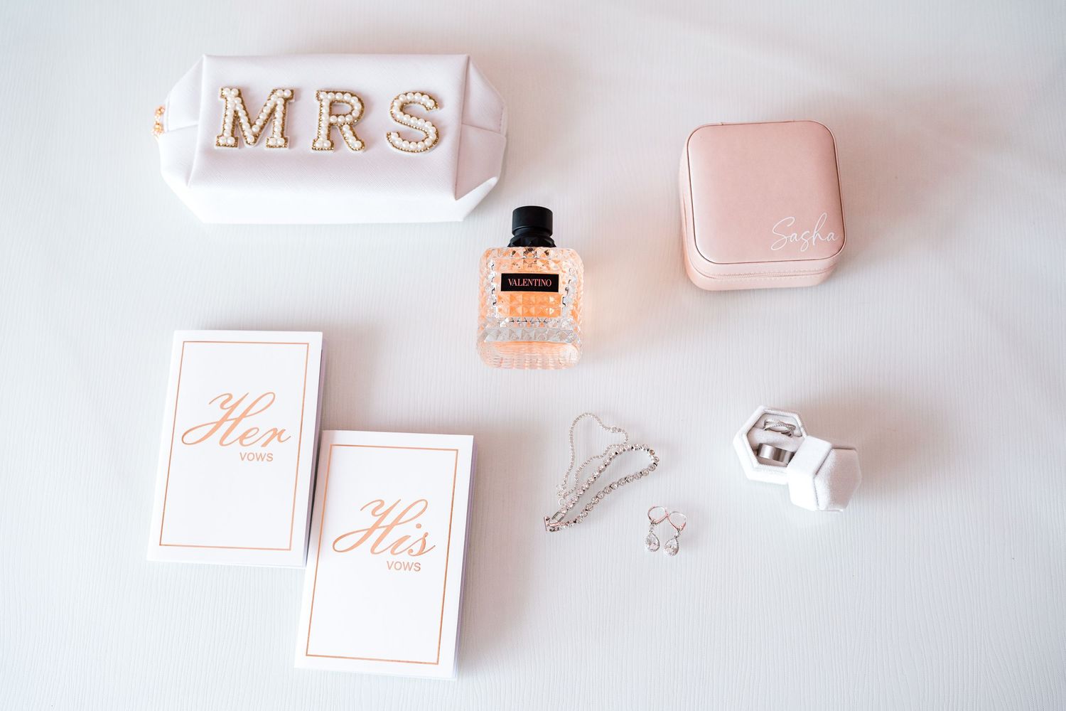 Wedding flat lay with MRS bag, perfume, ring box, and His and Hers vows.