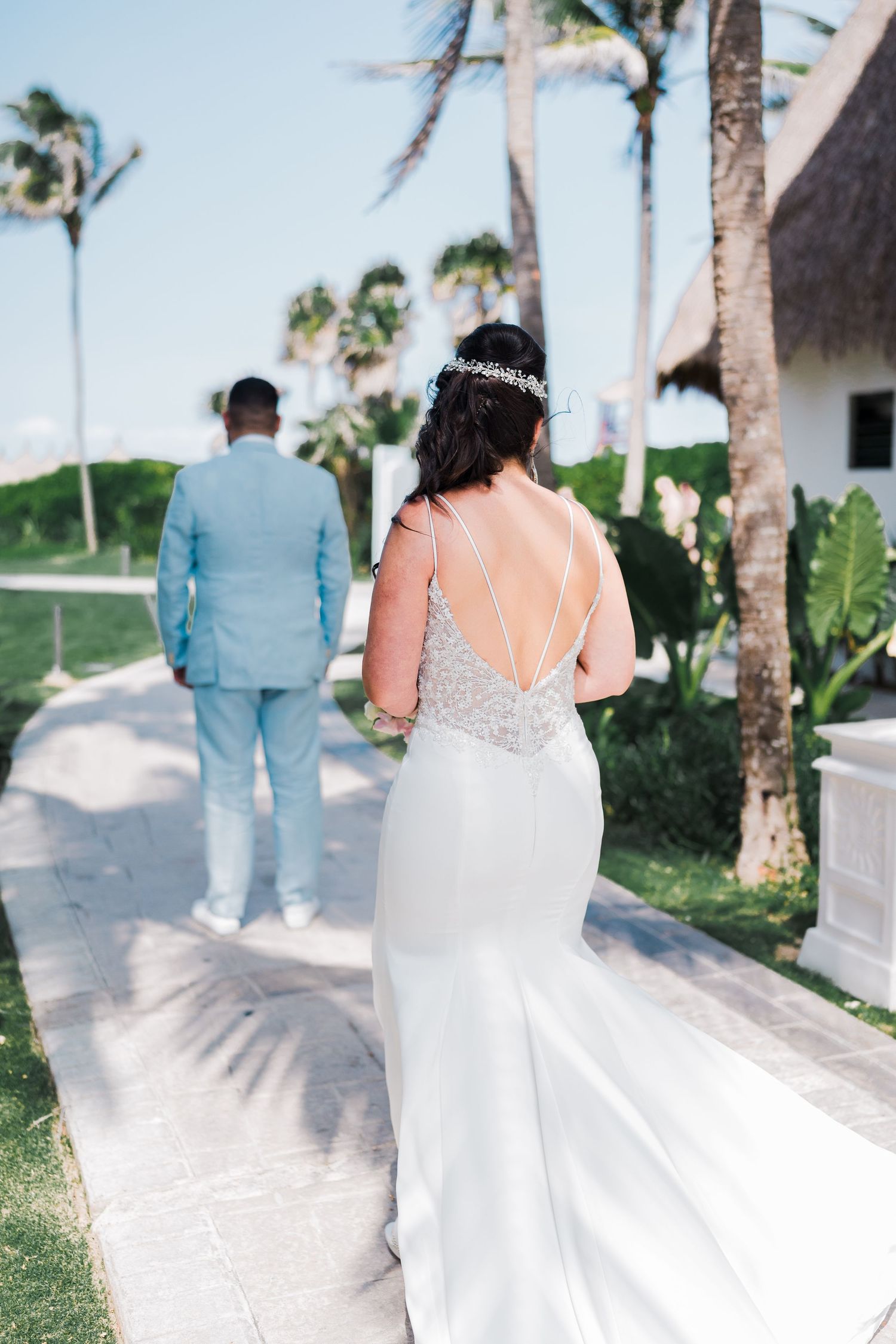 Bride in elegant backless wedding gown approaches groom in light blue suit for first look reveal.
