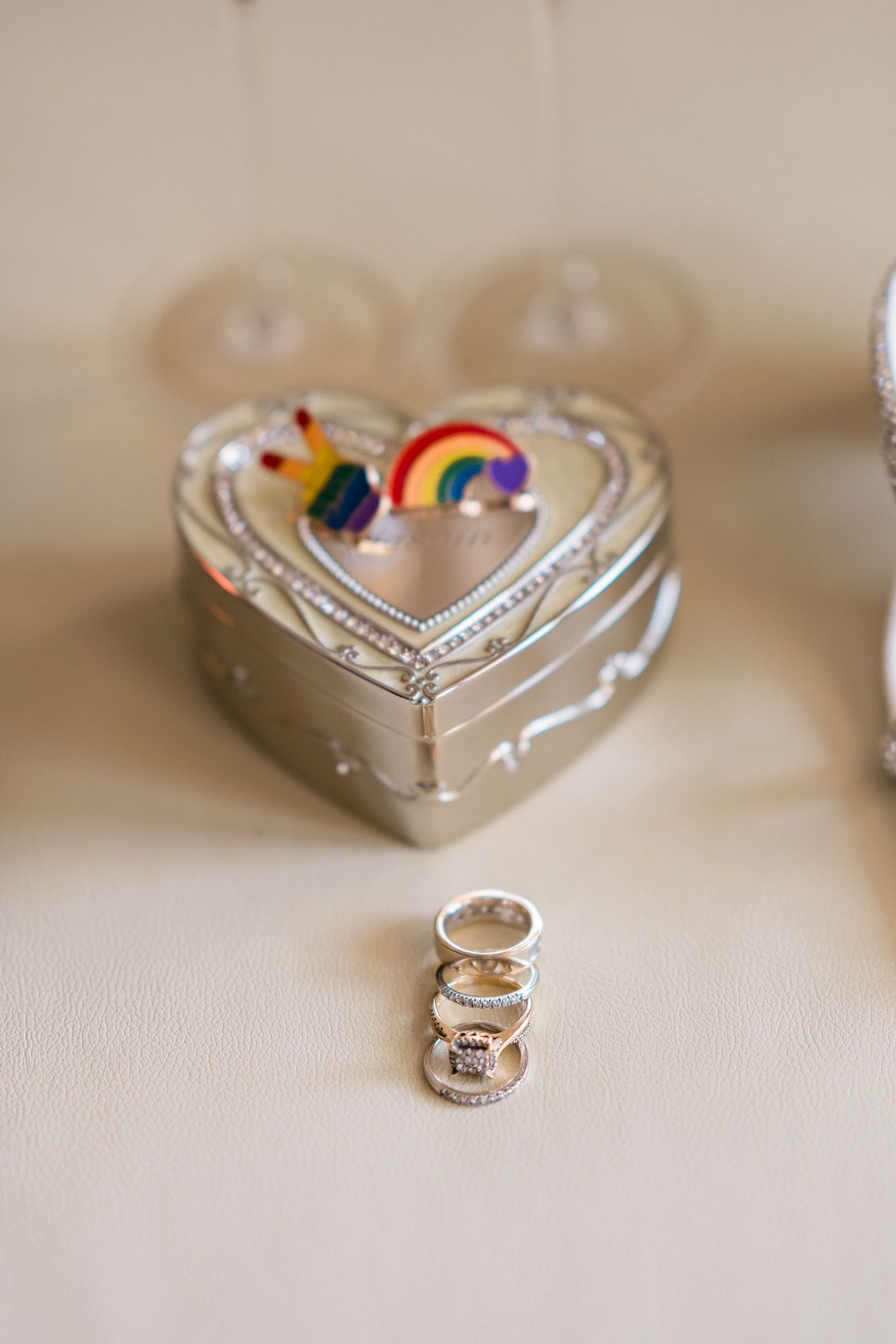 Wedding rings stacked before heart-shaped silver box with rainbow unicorn decoration.
