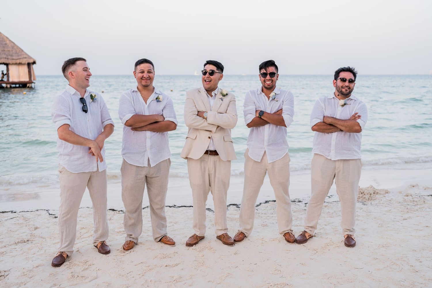 Groom with groomsmen in white shirts and tan pants posing on beach.