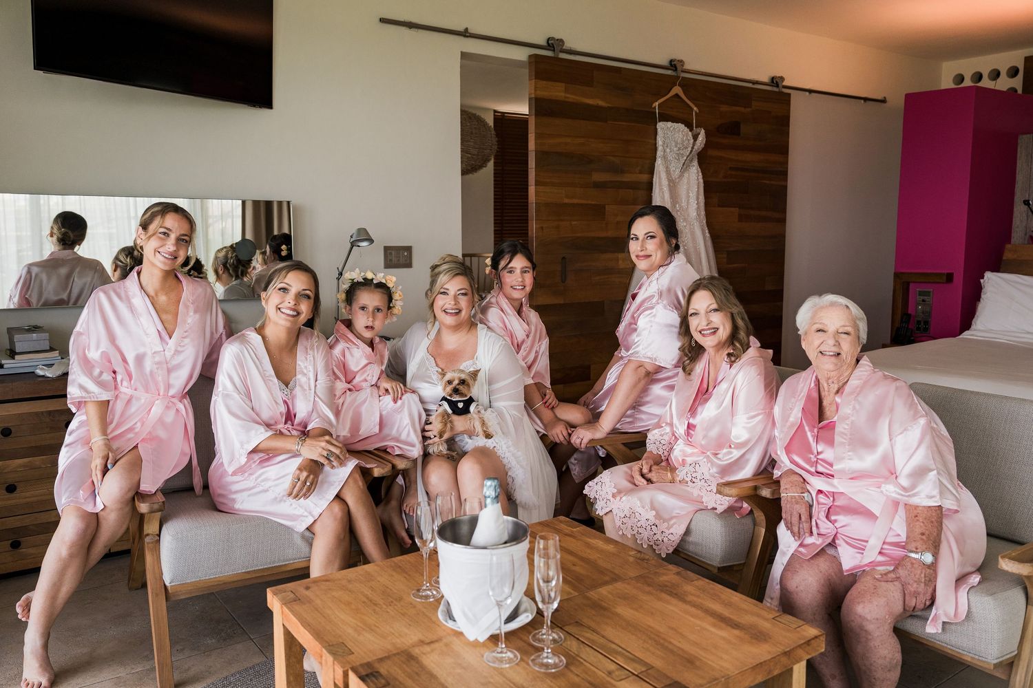Hotel Xcaret México Wedding  - Group of bridesmaids in matching pink satin robes gathered in a hotel room before a wedding ceremony.