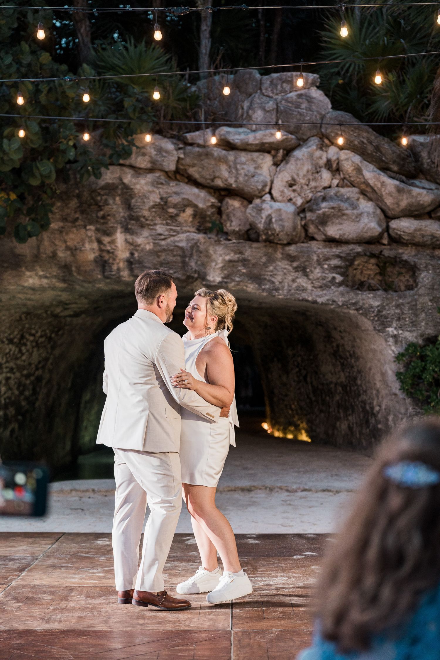 Hotel Xcaret México Couple sharing first dance outdoors at night near rocky cave backdrop with string lights at wedding reception.