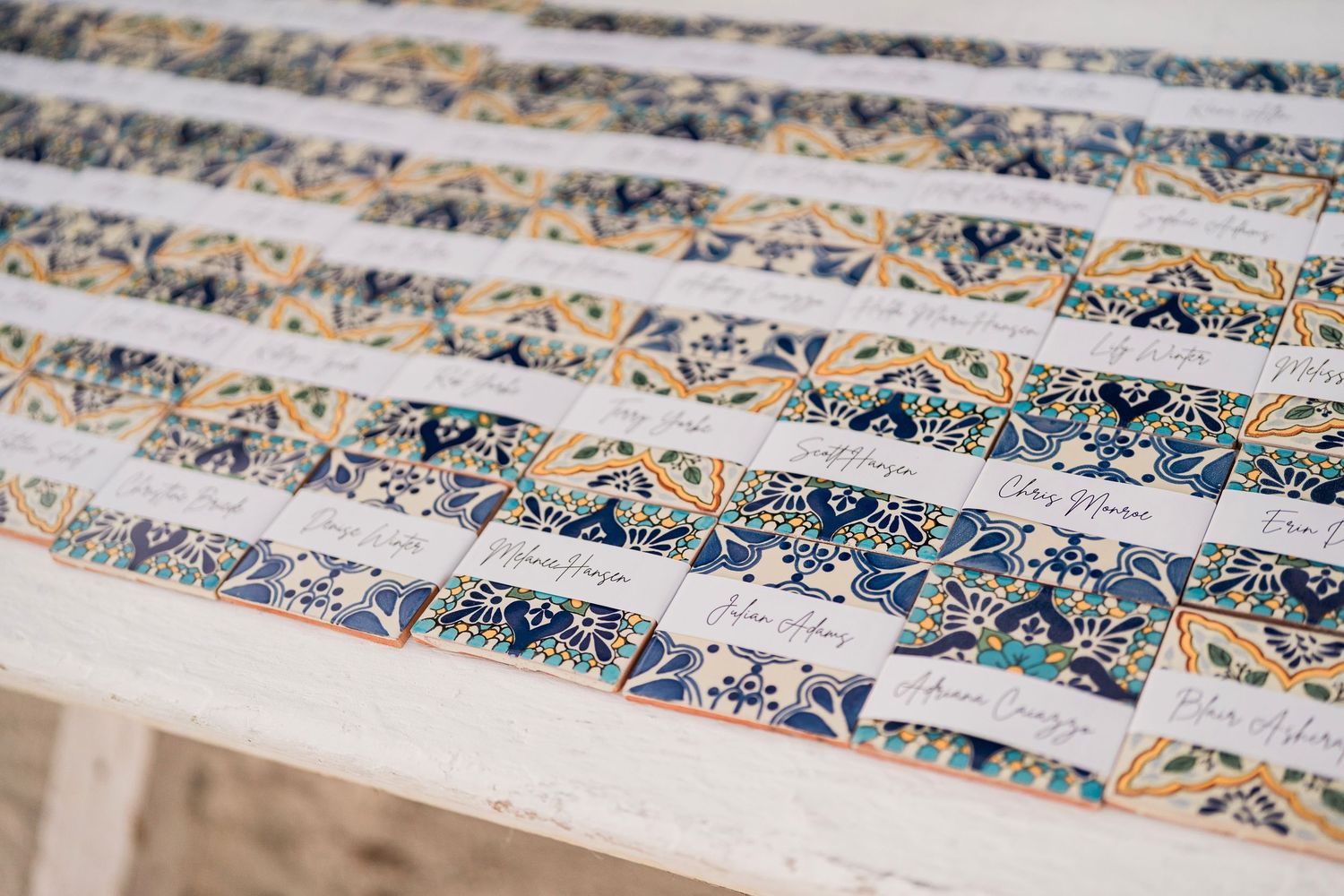 Rows of decorative wedding escort cards with blue and gold tile pattern design displayed on a white table.