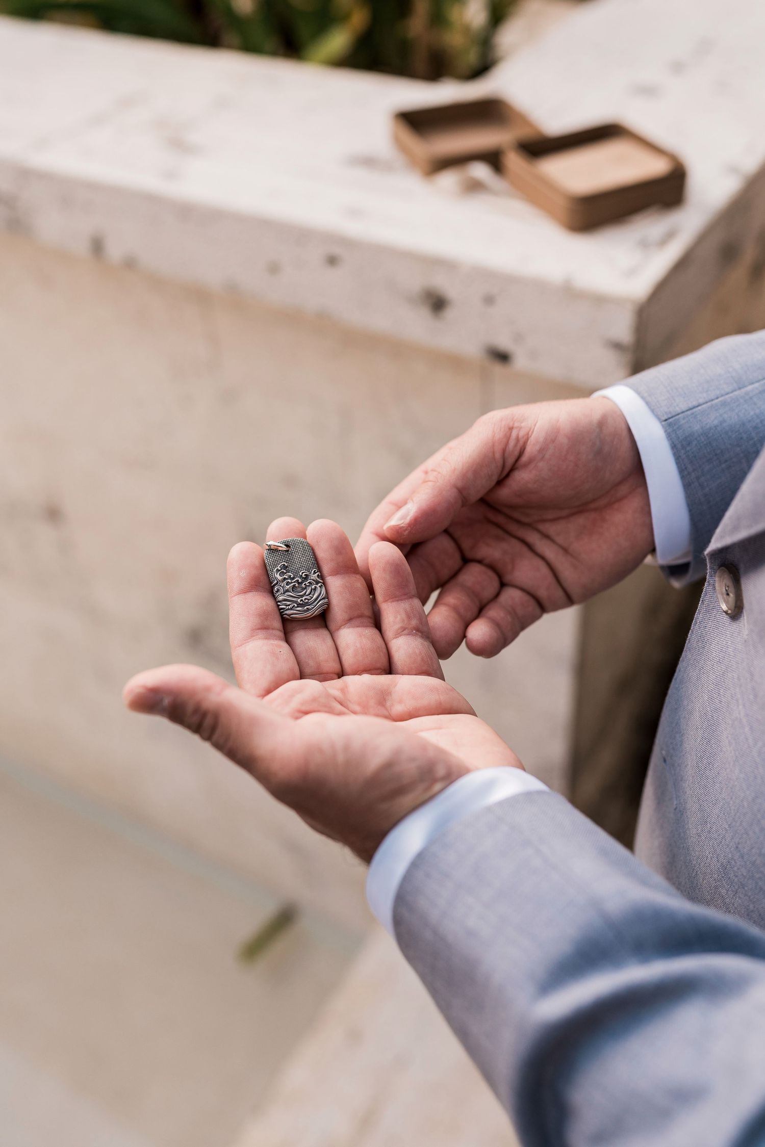 Man in suit holding a small engraved metal tag in his hands outdoors, with a wooden box in the background.