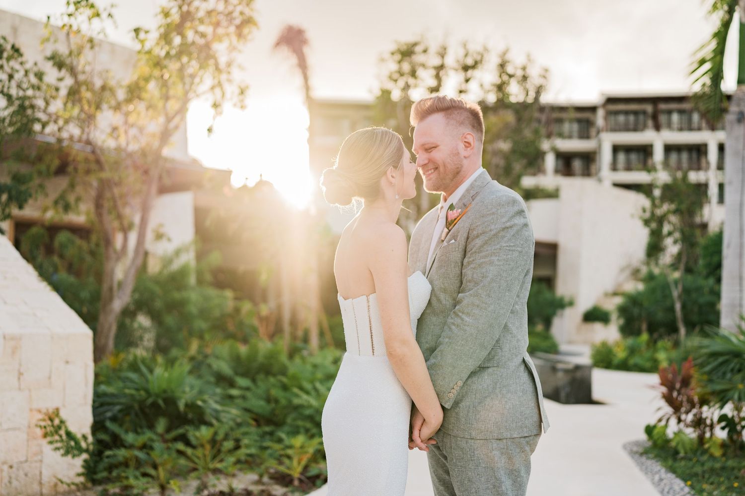 Bride and groom share a romantic moment at sunset, with golden light glowing behind them in a lush garden setting.