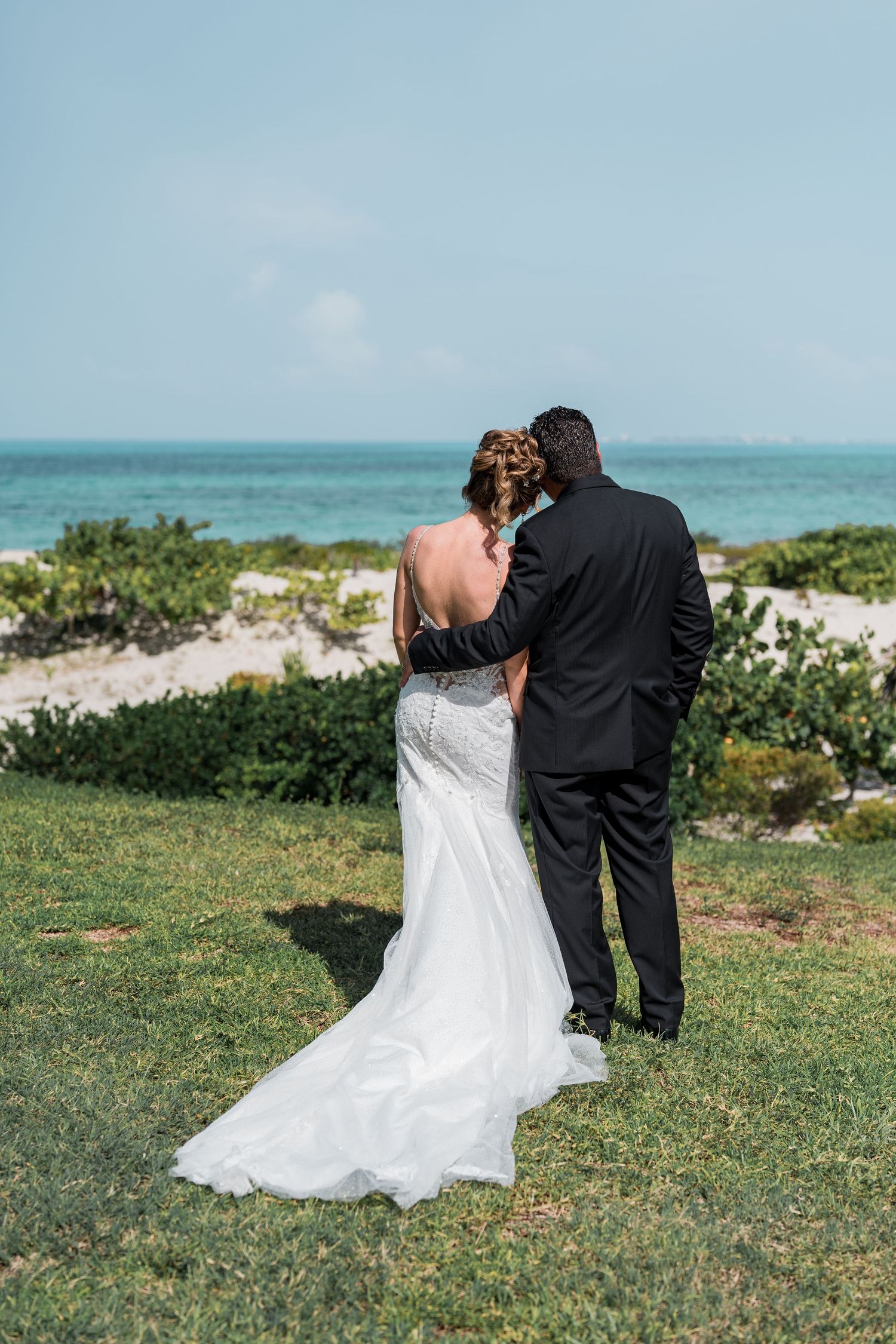 Bride and groom stand together gazing at turquoise ocean views during their beach wedding in Mexico.