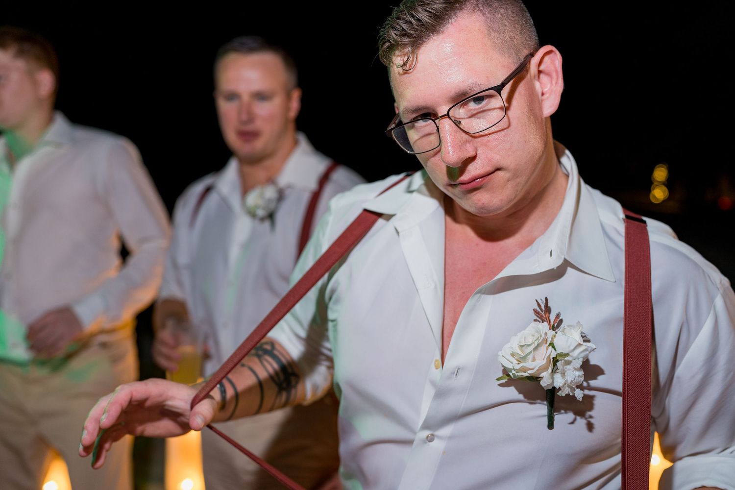 Groomsman in white shirt with suspenders and boutonniere posing at beach wedding reception.