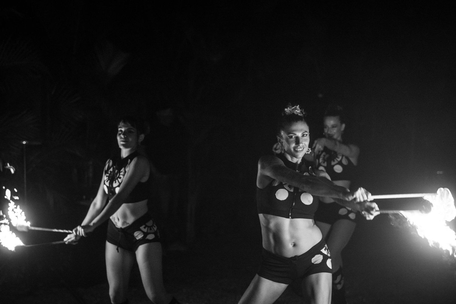 Black and white photo of two female fire dancers performing with flaming batons at a wedding.