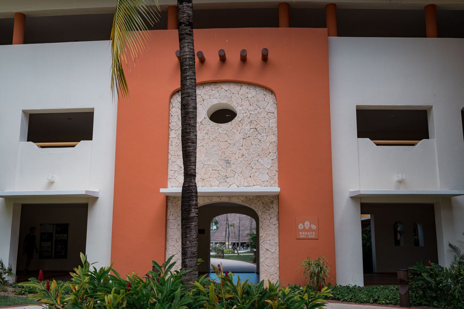 Exterior view of a terracotta orange resort building with an arched entryway and tropical landscaping.