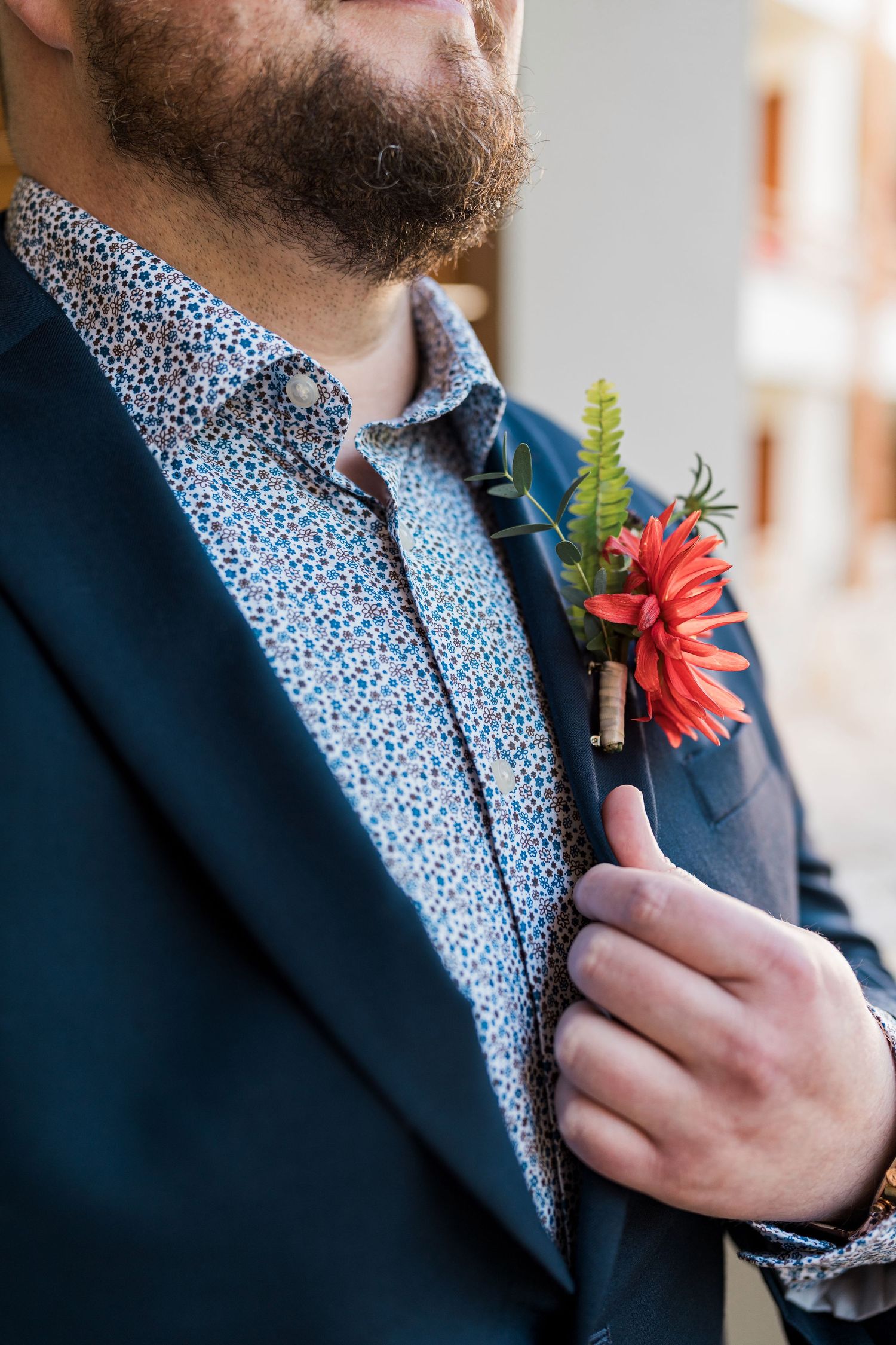Secrets Akumal Wedding - Bearded groom in navy blazer and floral shirt holds a red dahlia boutonniere with greenery on his lapel.