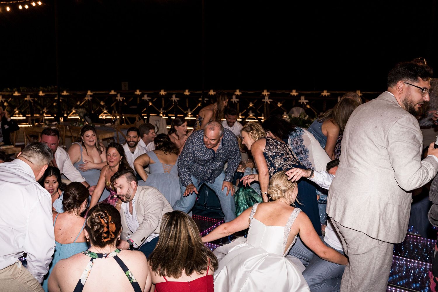 Wedding guests gathered on the dance floor at an outdoor nighttime reception celebration.