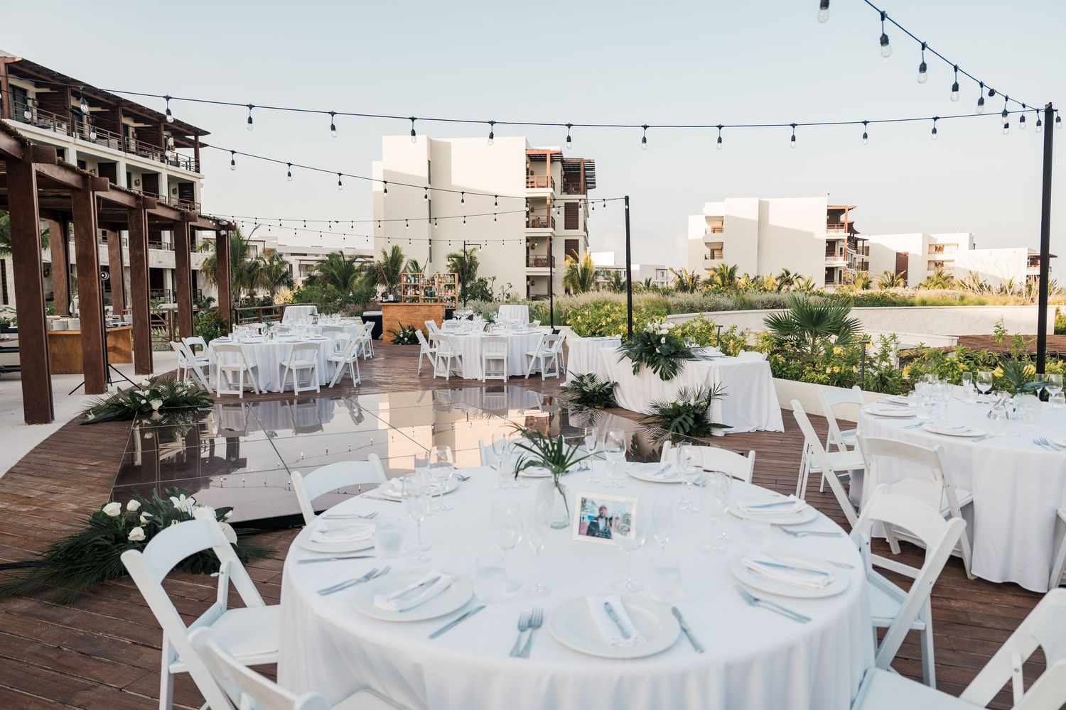 Elegant outdoor wedding reception with white round tables, string lights, and lush greenery at a beachside resort venue.