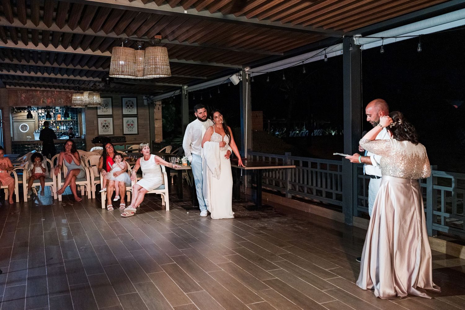Wedding party gathered on a rustic wooden venue deck as a guest delivers a heartfelt speech.