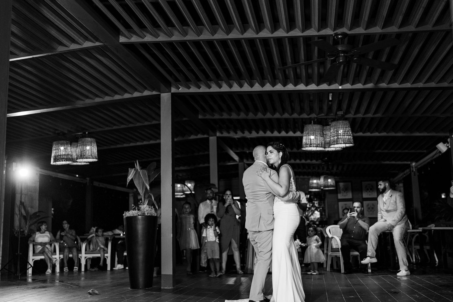 Black and white photo of bride and groom dancing at wedding reception with guests watching in background.