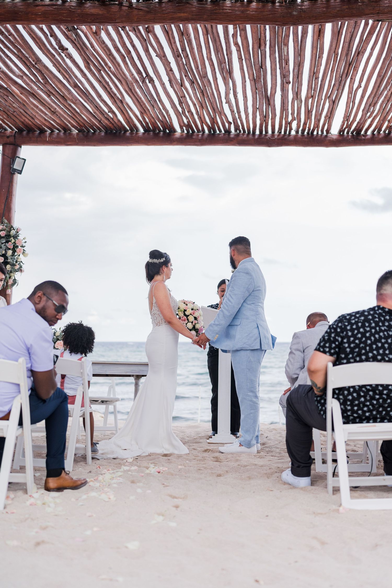 Bride and groom exchange vows at romantic oceanfront beach wedding ceremony under wooden pergola.