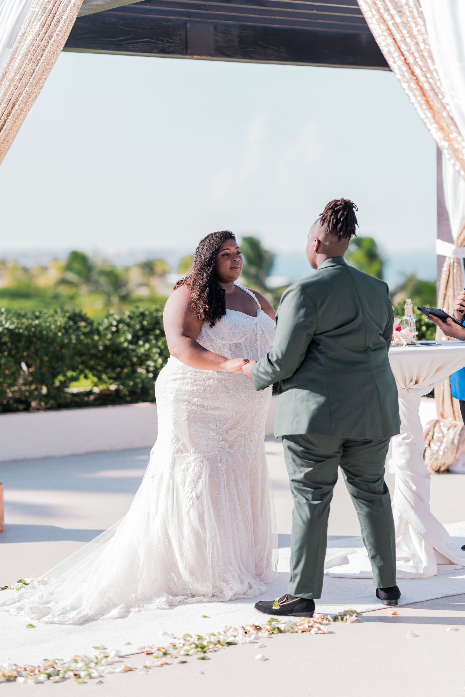Bride and groom holding hands during wedding ceremony under elegant outdoor pergola.