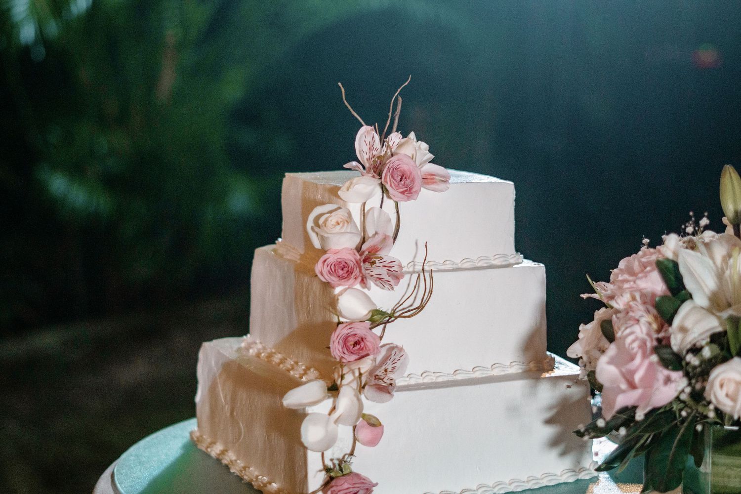 Close-up of a white square wedding cake decorated with pink roses and delicate floral sugar decorations.