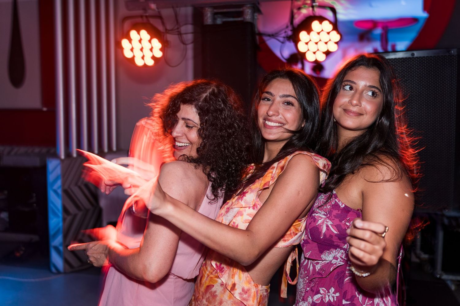 Three young women smiling and dancing together at a vibrant party event.