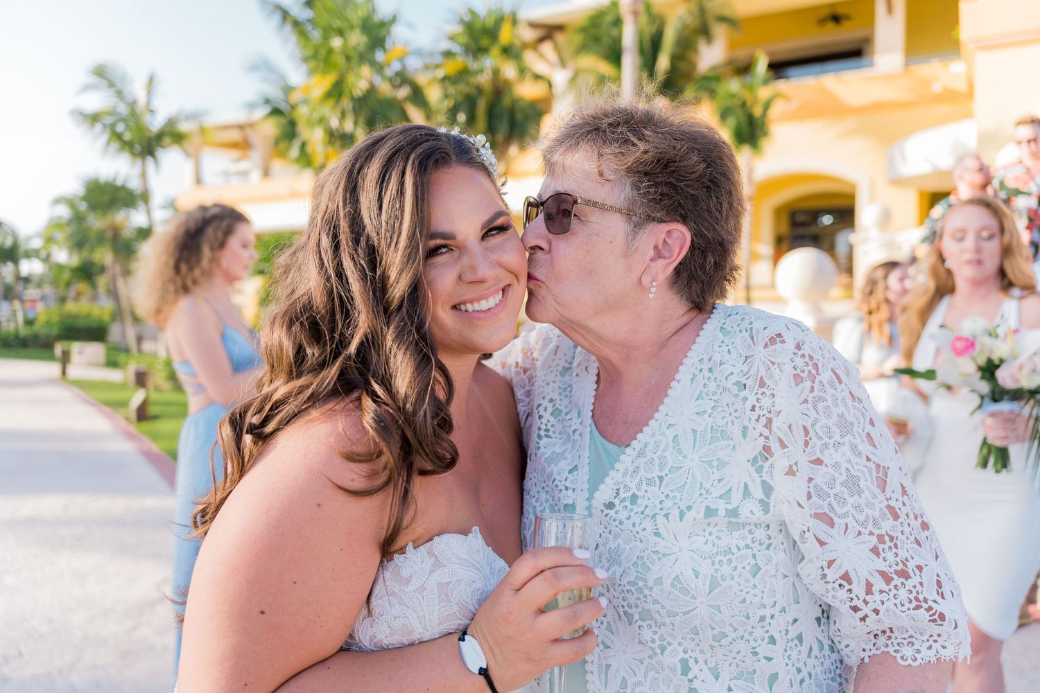 Elderly woman kissing a smiling bride on the cheek at a beautiful outdoor beach wedding.