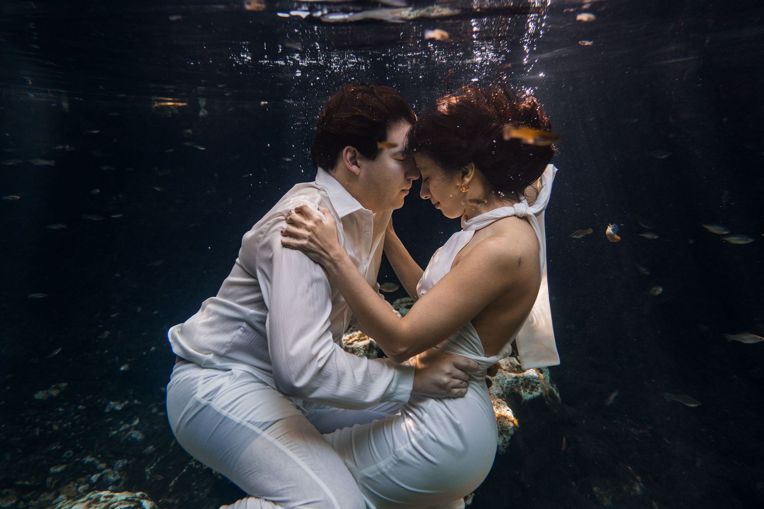 Couple sharing a romantic underwater kiss in white wedding attire, surrounded by water in a dreamy aquatic setting.