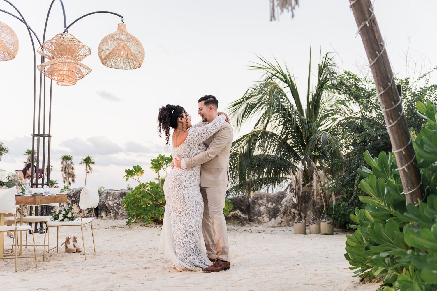 Xcaret Arte Wedding - Bride and groom share first dance on sandy beach surrounded by palm trees and boho decor at tropical wedding.