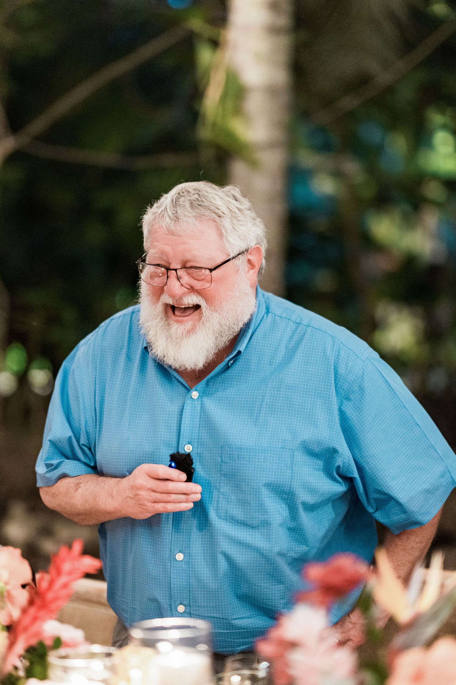 Secrets Akumal Wedding - Smiling elderly man with white beard and glasses wearing a blue shirt at an outdoor tropical event.