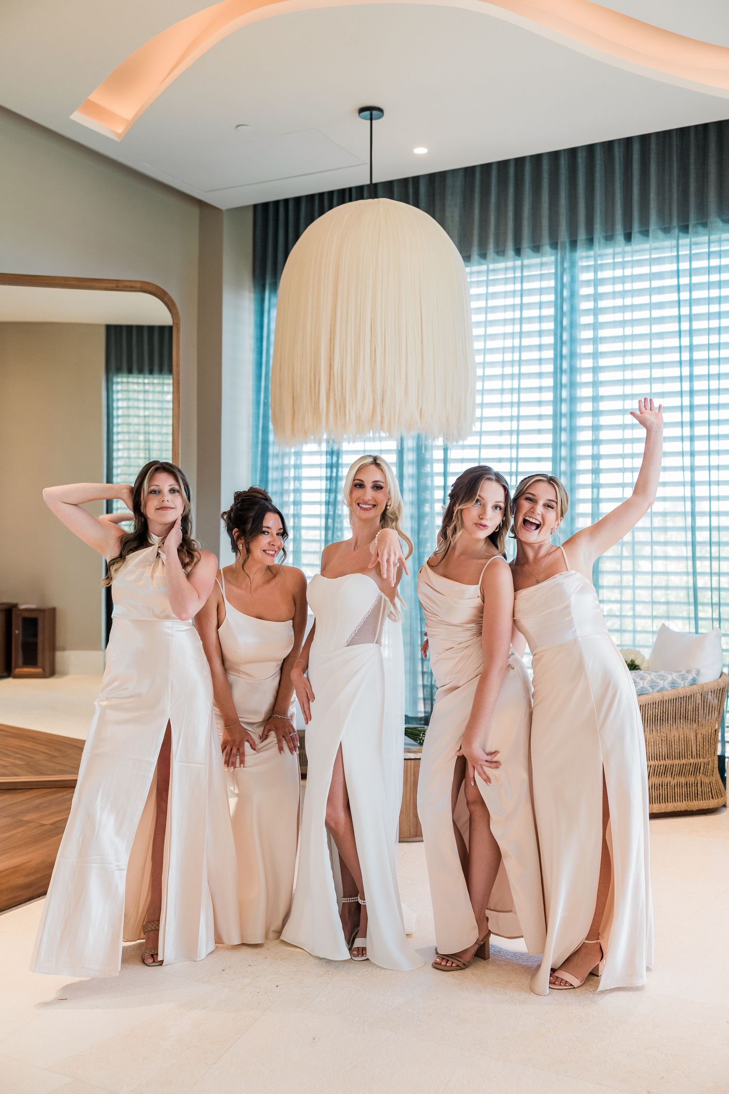 Bride and four bridesmaids in matching champagne satin gowns posing and celebrating together joyfully.