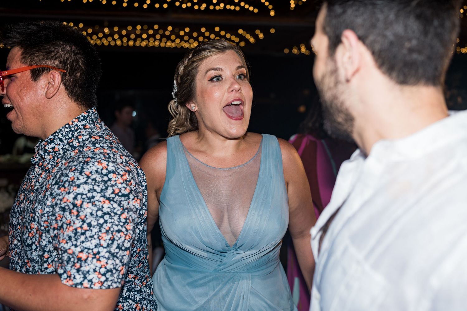 Excited wedding guest in blue dress laughing and socializing at a festive outdoor reception.