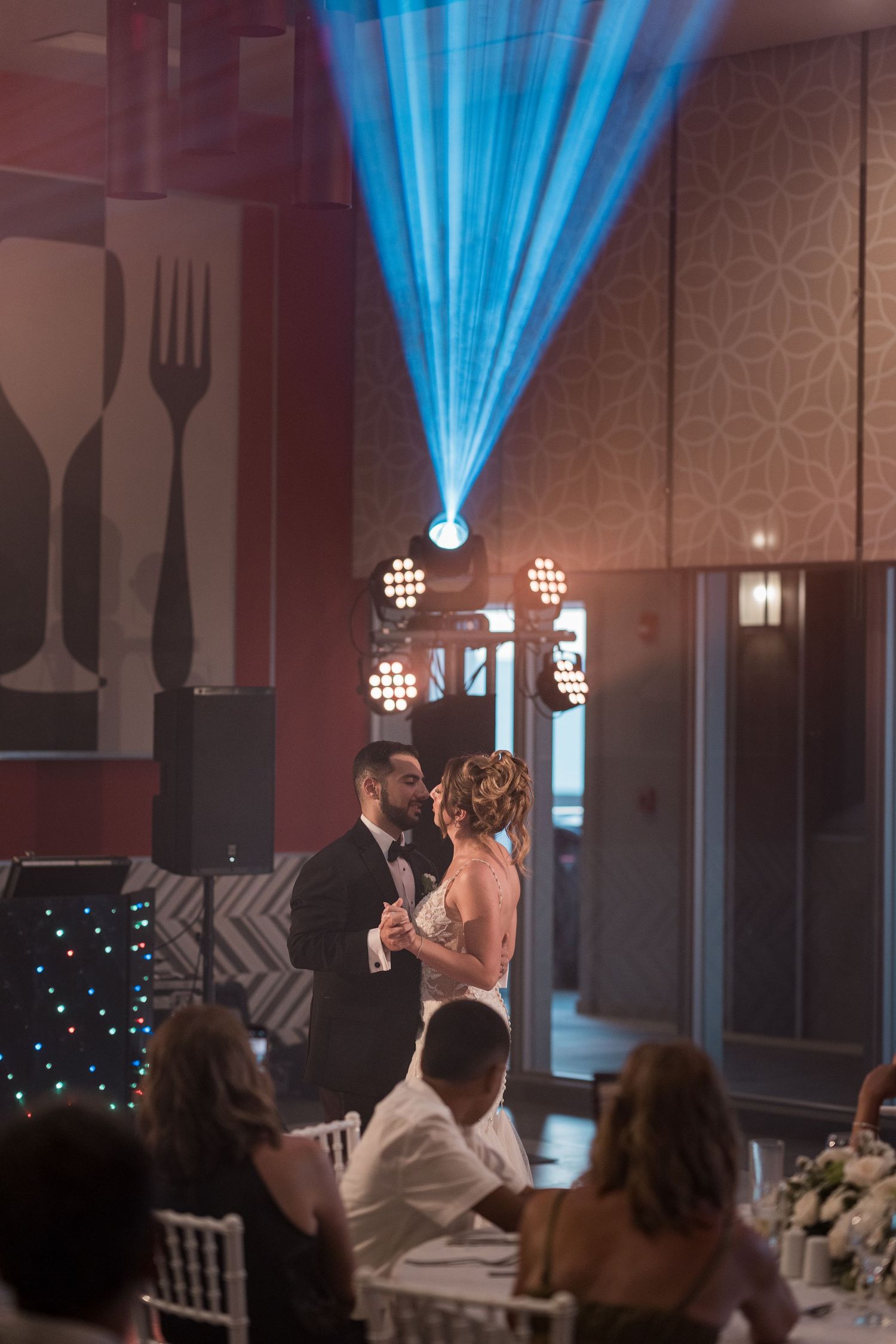 Bride and groom share first dance under dramatic blue spotlight beams in elegant reception venue.